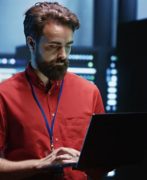 Home de barba e camisa vermelha segurando um notebook